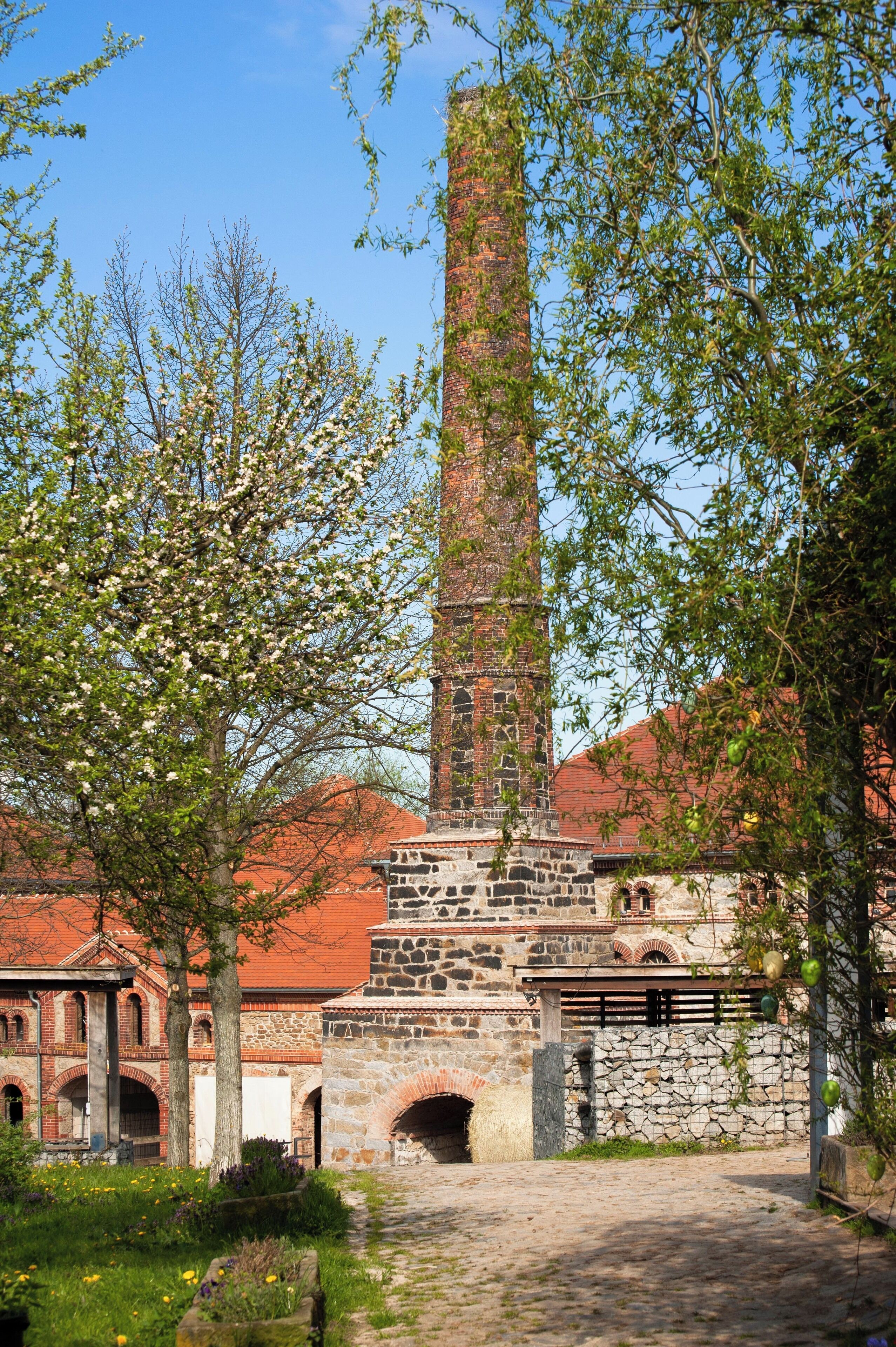 Een historisch gebouw met een hoge bakstenen toren, stenen bogen en een geplaveid pad.