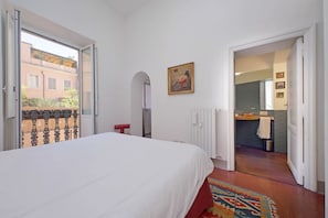 Un dormitorio con una cama, una ventana, una puerta que da a un baño y un cuadro en la pared.