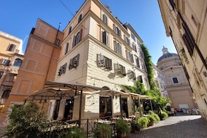 Una calle estrecha con un patio de café, un edificio con cúpula y otro edificio con balcón.