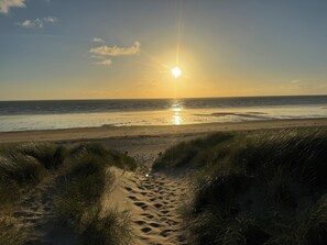 Ein Strandweg, der zum Meer führt, mit untergehender Sonne im Hintergrund.