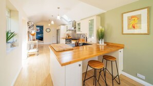 A modern kitchen with a wooden island, bar stools, and a view into the dining area. - Fountainhall Townhouse, Aberdeen (Aberdeen City)