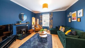 A living room with a fireplace, a green sofa, a round coffee table, and a blue accent wall.