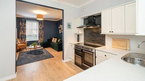 A modern kitchen with white cabinets, a built-in stove, and a large window with curtains.