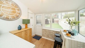 A modern kitchen with a large wooden clock, a dining area with a table set for two, and a view of a garden through large windows.