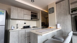 A modern kitchen with grey cabinetry, a microwave, a gas stove, and a built-in oven. There is a small seating area with a grey chair and a table. - APARTMENT NEAR PROVENZA BY HOOST 2410 (Medellín)
