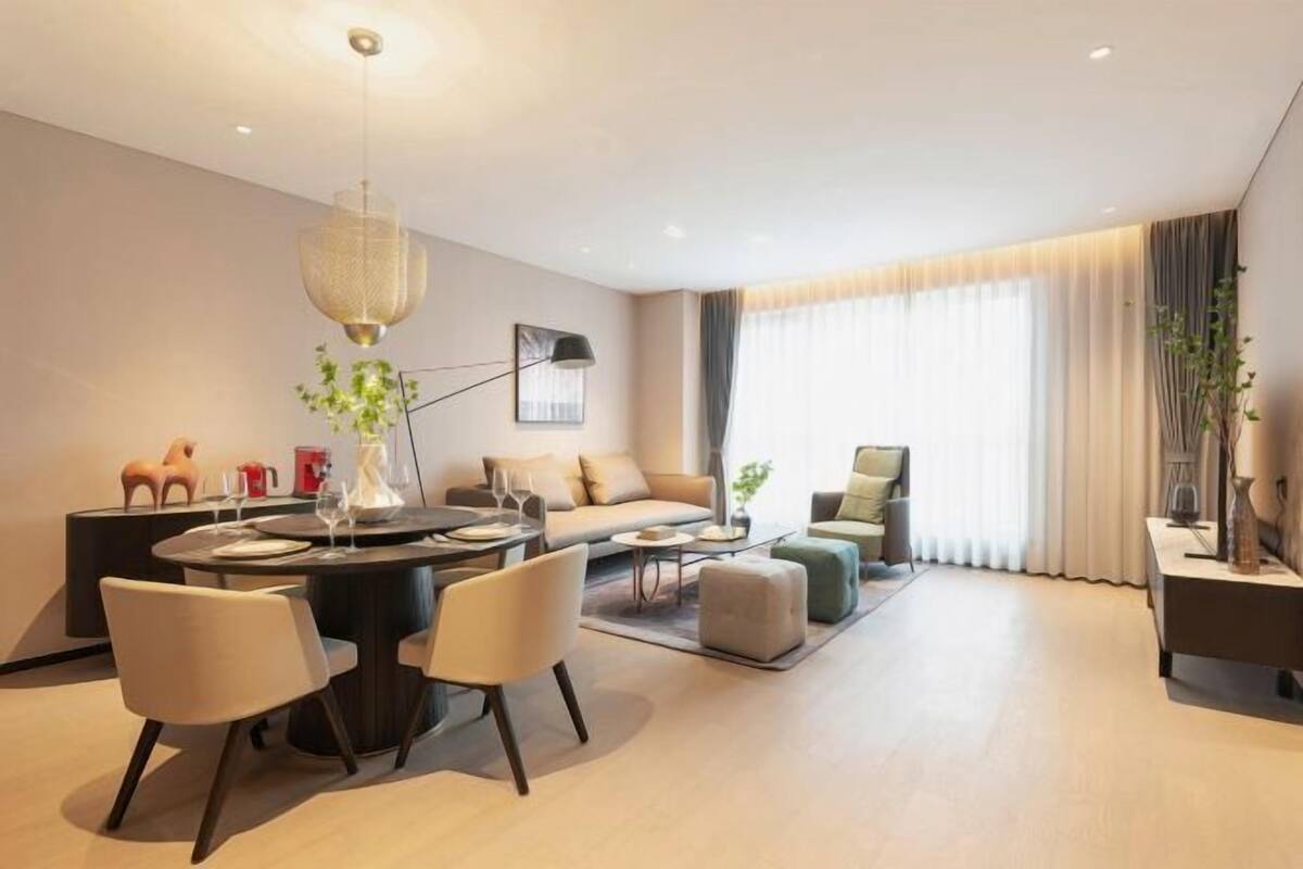 A modern living room with a round dining table, sofas, and a large window with curtains.