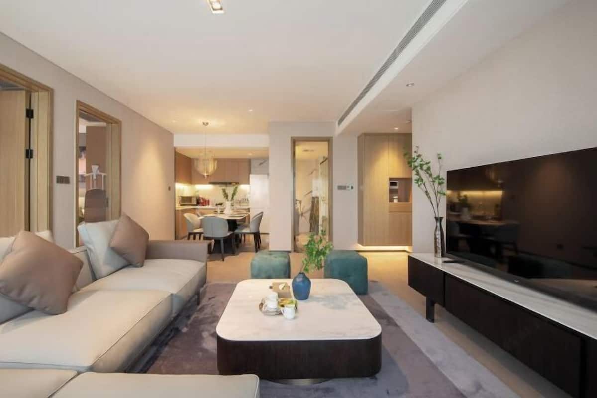 A modern living room with a sofa, a coffee table, and a TV. There is a dining area in the background.