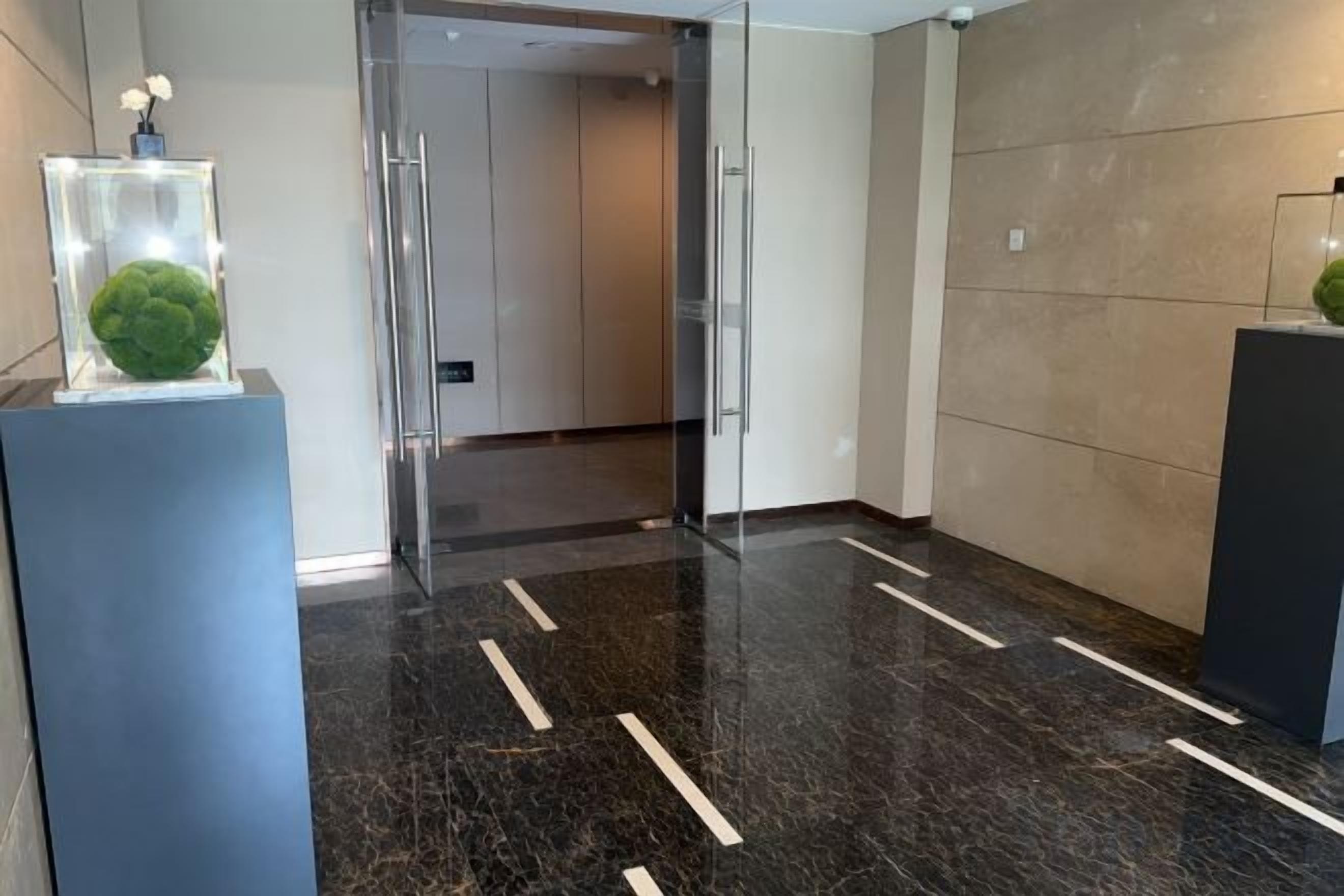 A modern lobby with a glass door entrance, a marble floor with white lines, and a beige wall.