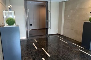 A modern lobby with a glass door entrance, a marble floor with white lines, and a beige wall. - ANEASY RESIDENCE (Chengdu)