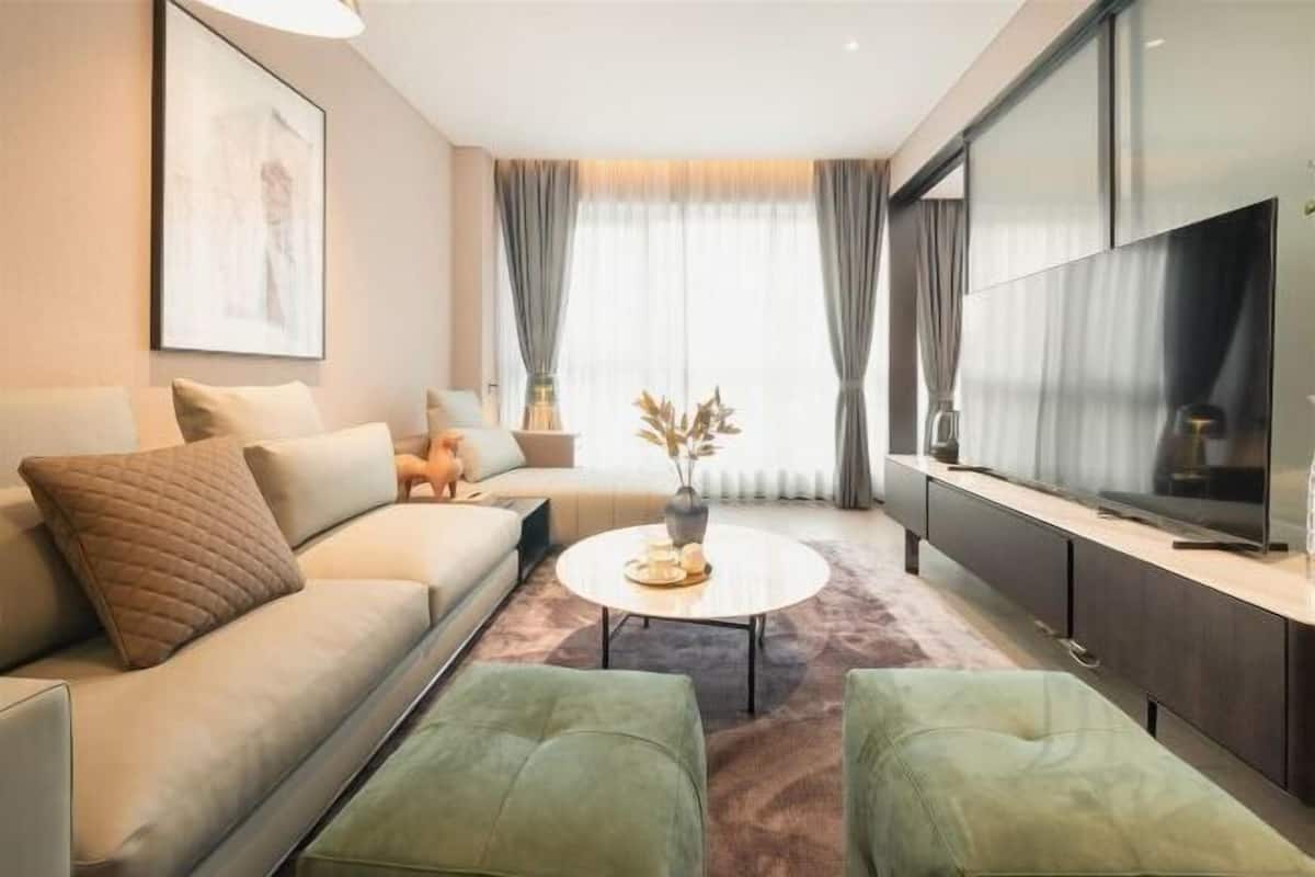 A modern living room with a sofa, ottomans, a coffee table, and a flat-screen TV.