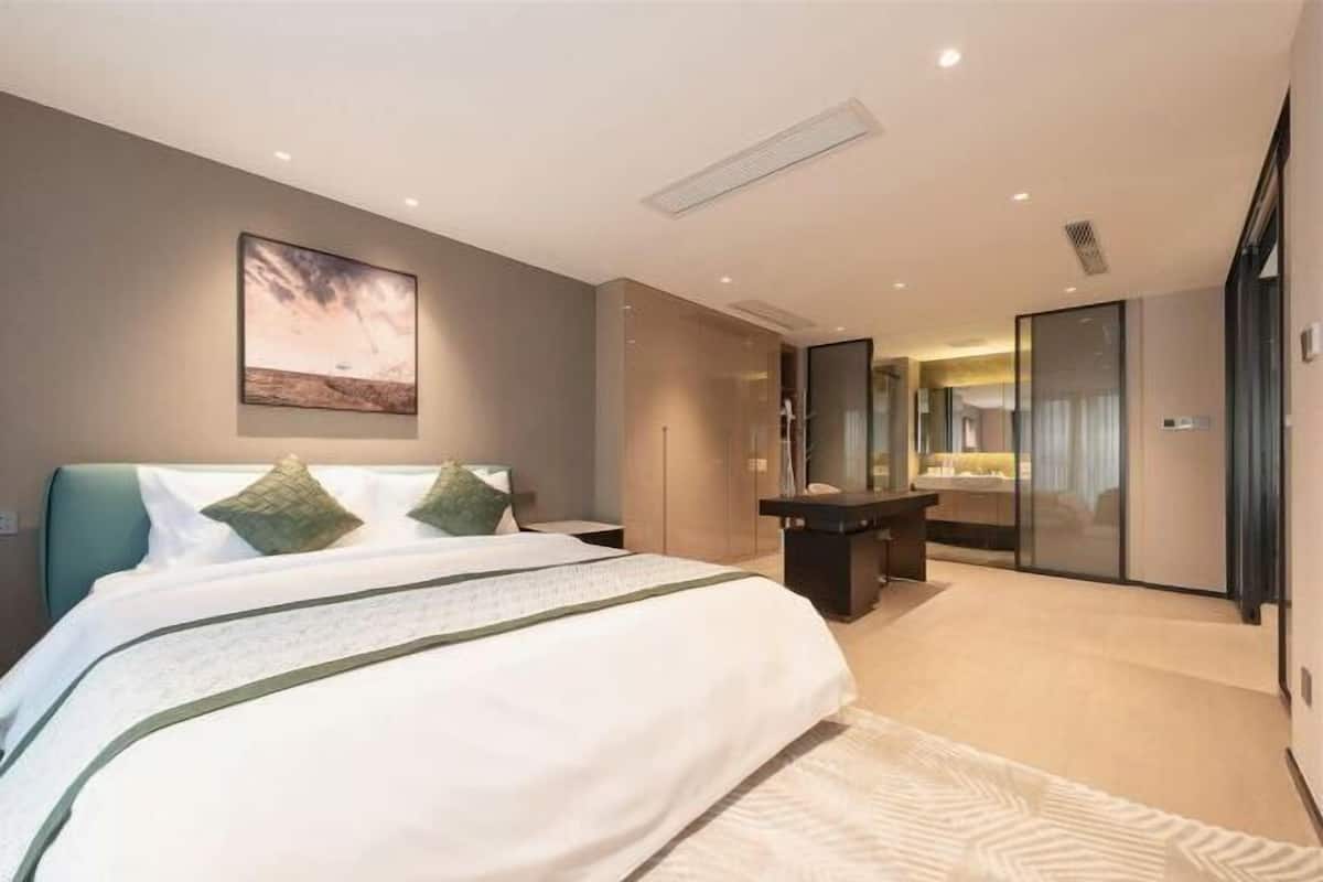 A modern hotel room with a large bed, a desk, and a glass partition.