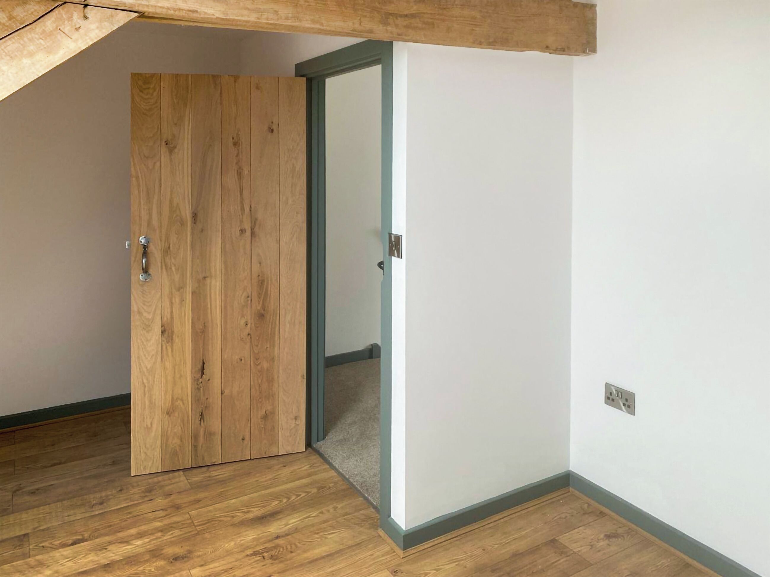 Una stanza con una porta in legno, un muro bianco e un pavimento in legno.