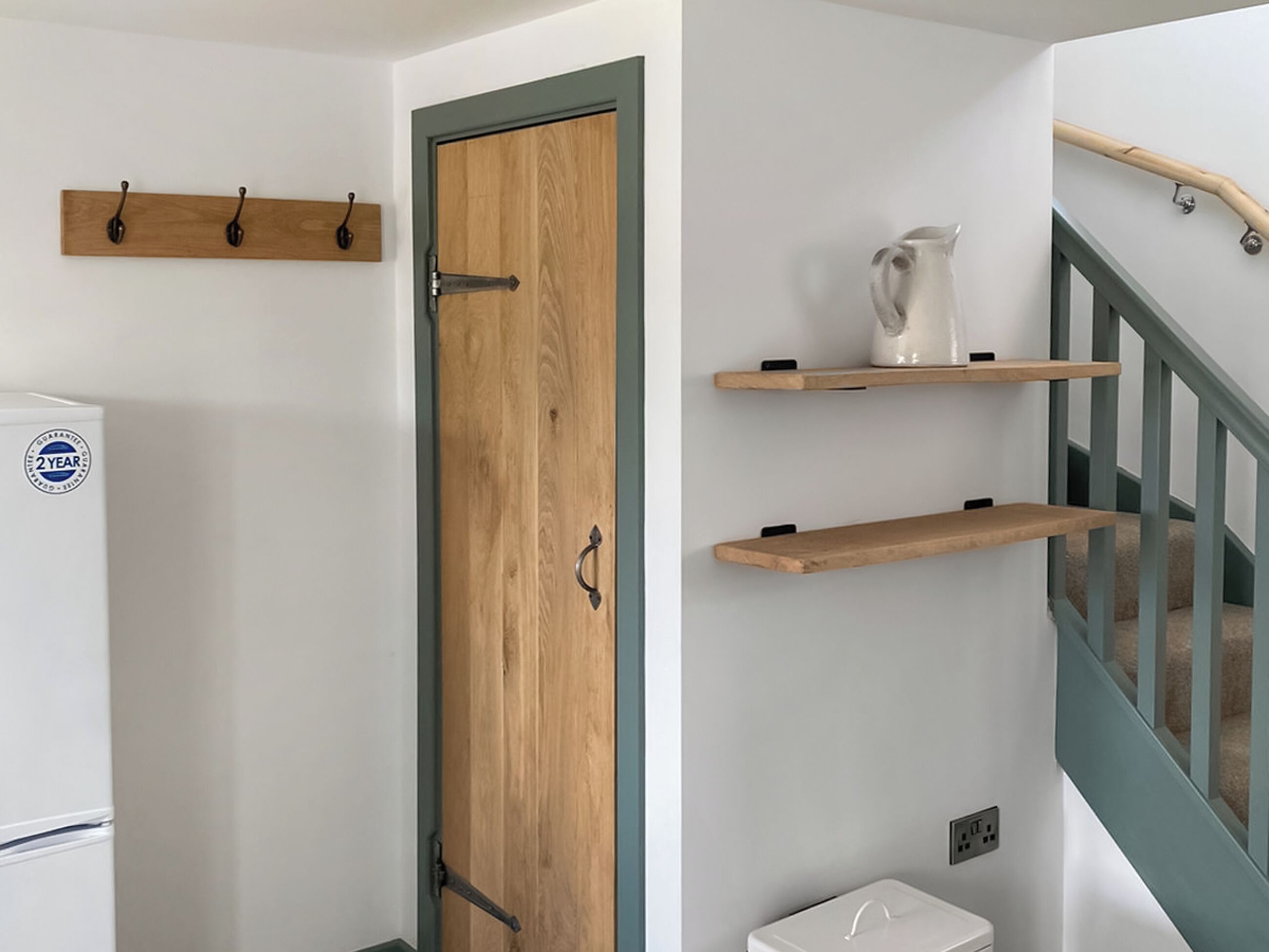 Ein Zimmer mit Holztür, einem weißen Kühlschrank und einer Treppe mit blauer Handlauf.
