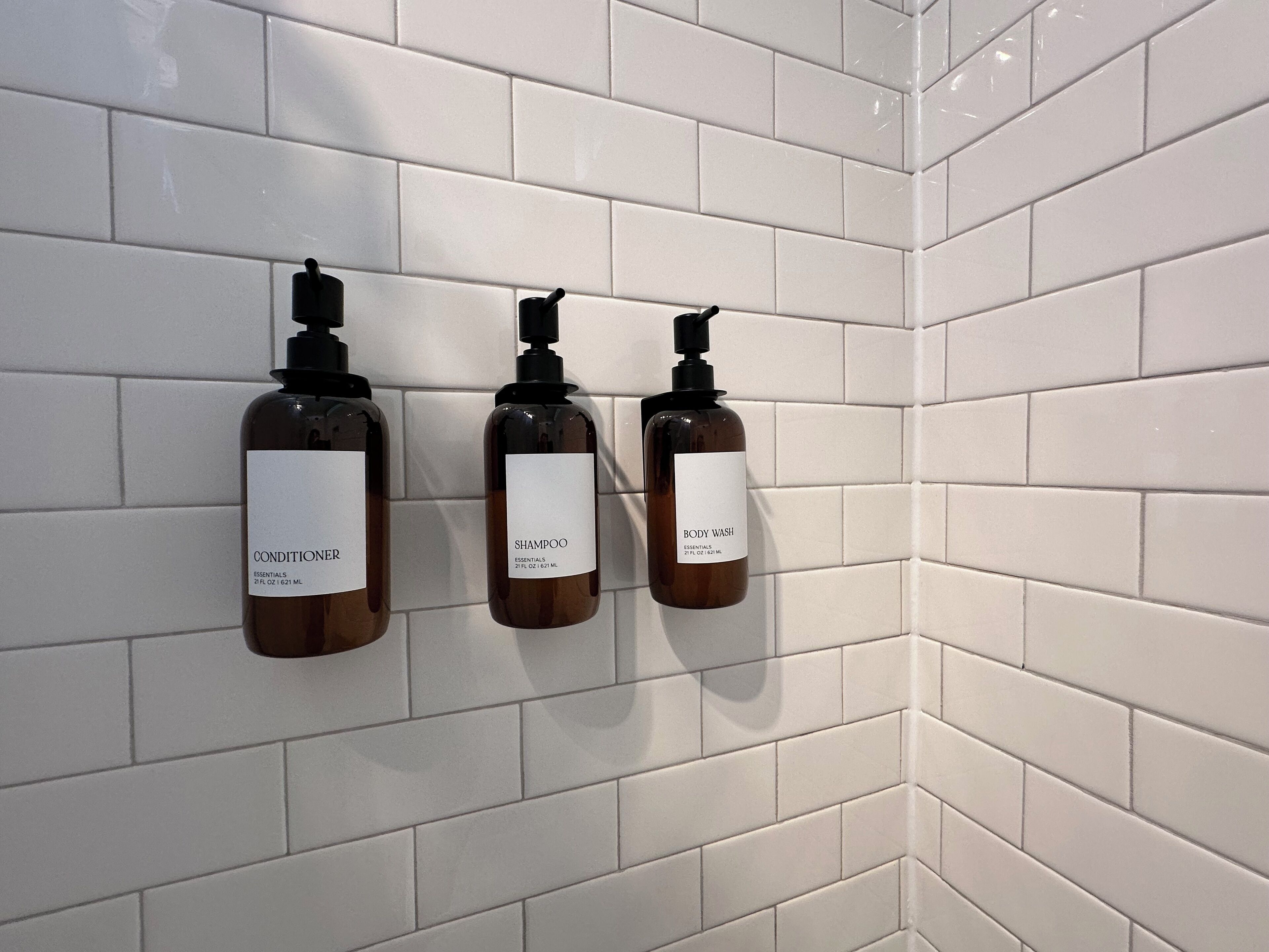 Tre flasker bodywash og balsam hænger på en hvid flisevæg.