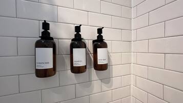 Tre flasker bodywash og balsam hænger på en hvid flisevæg.
