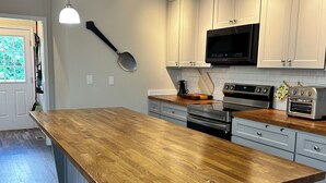 A modern kitchen with a large wooden island, white cabinets, stainless steel appliances, and pendant lighting.