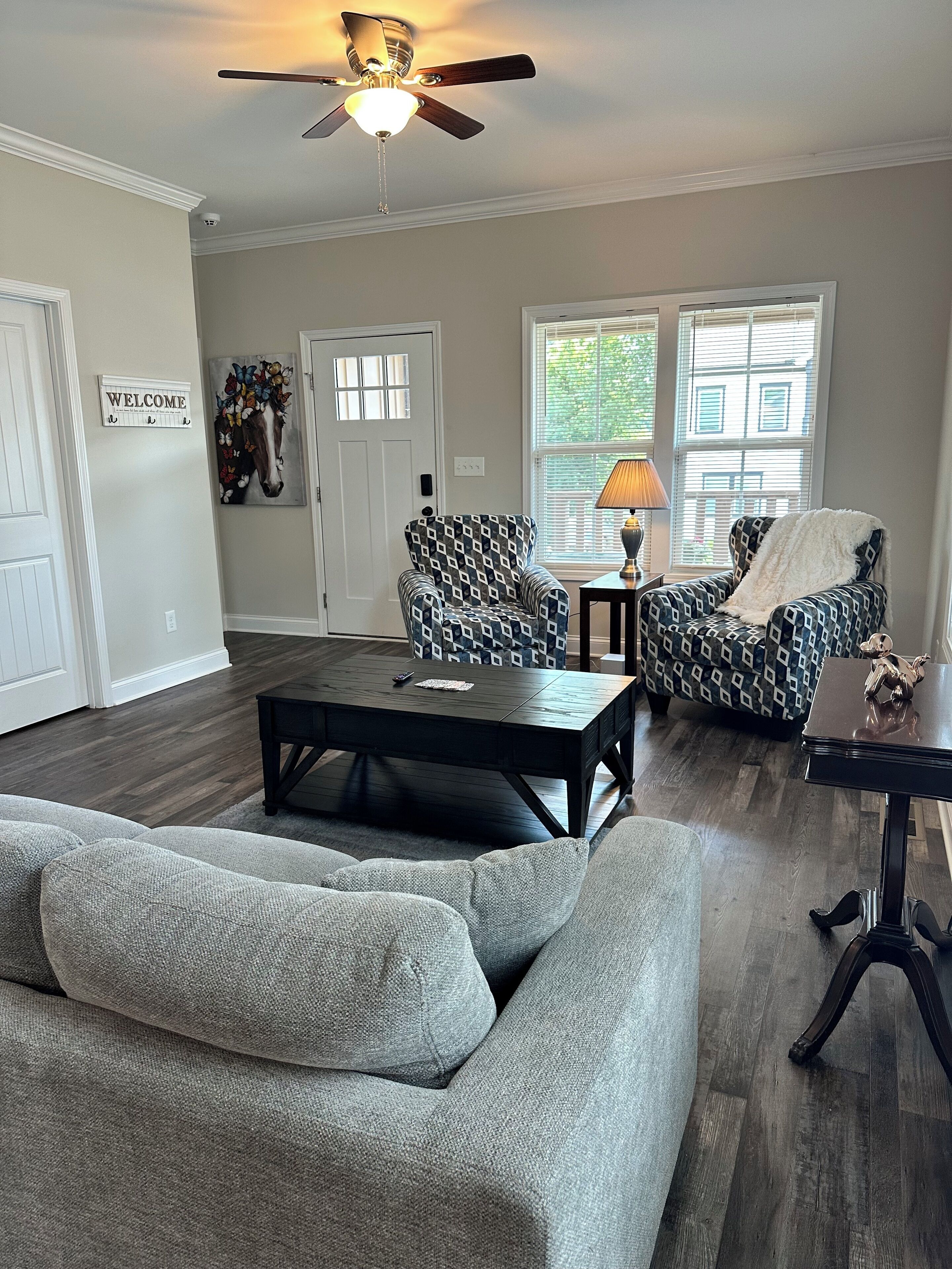 A living room with a sofa, two patterned armchairs, a coffee table, and a ceiling fan.
