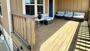 A covered porch with a wooden ceiling, a seating area with cushions, and a small table with a potted plant.