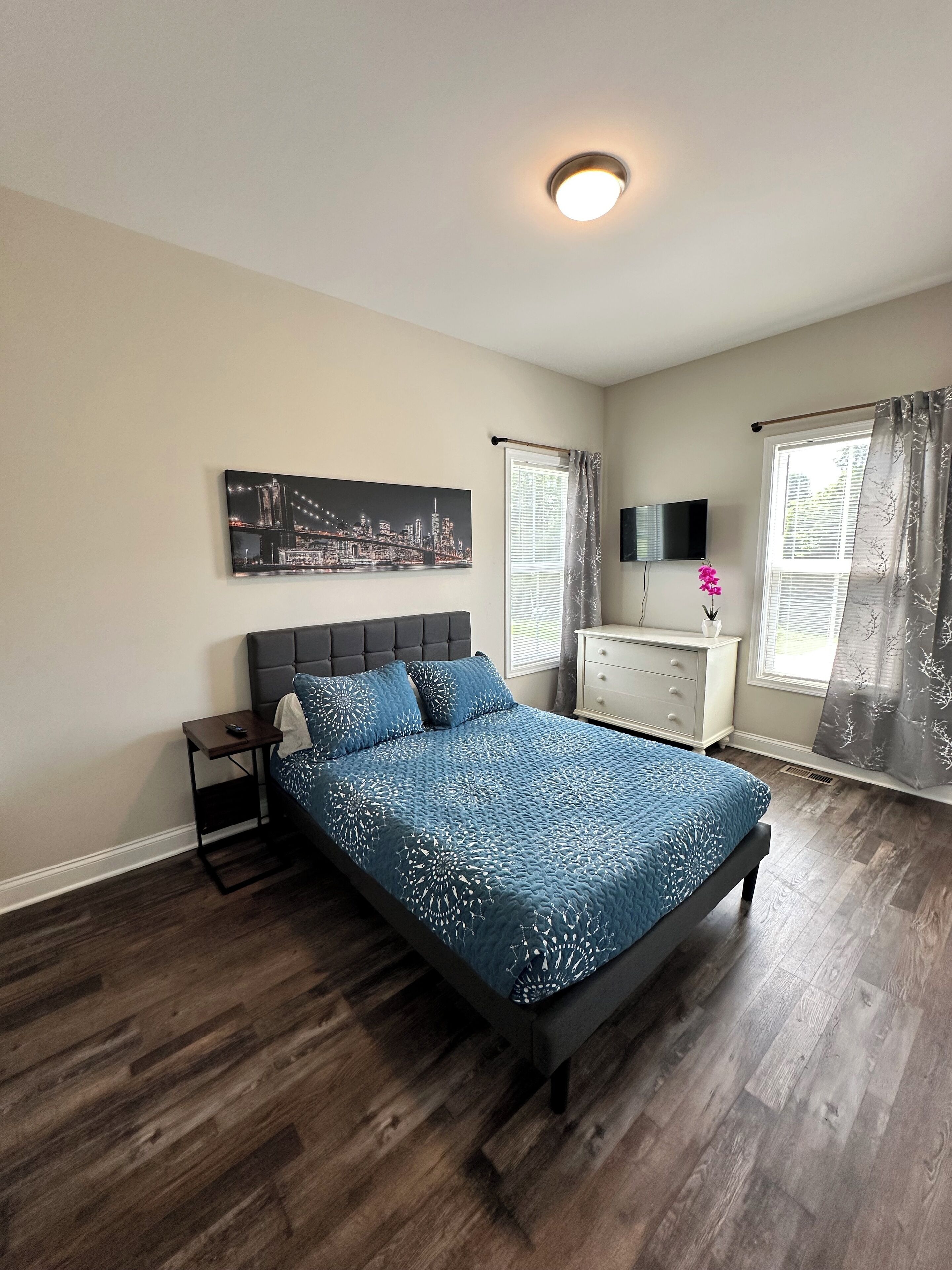 Una camera da letto con un letto, un comodino, una cassettiera, una televisione e un dipinto con una vista sulla città.