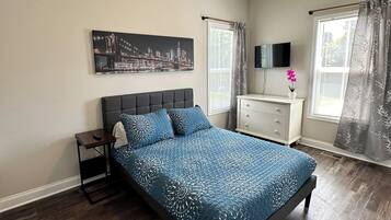 Una camera da letto con un letto, un comodino, una cassettiera, una televisione e un dipinto con una vista sulla città.