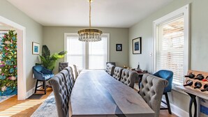 Een eetzaal met een lange tafel, stoelen, een kroonluchter, een kerstboom en een wijnrek.