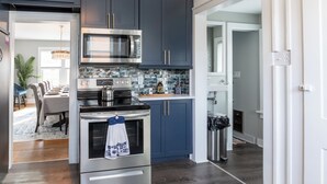 Een moderne keuken met donkerblauwe kastjes, roestvrijstalen apparatuur en een betegelde achterwand.