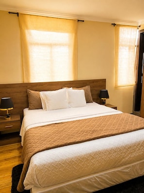 A hotel room with a large bed, two bedside tables with lamps, a wooden headboard, and curtains on the windows. - Melody Hotel (Cuenca)