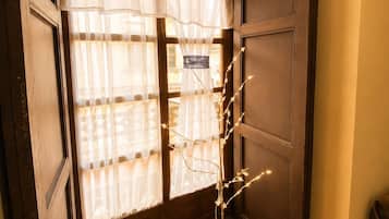 A room with a wooden floor, a window with sheer curtains, and a decorative light stand.