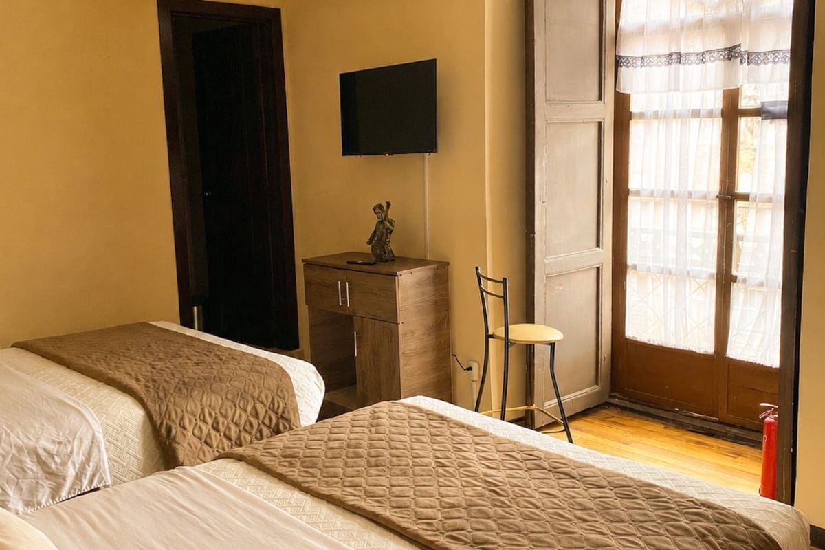 A hotel room with two beds, a television, a small table, and a window with curtains.