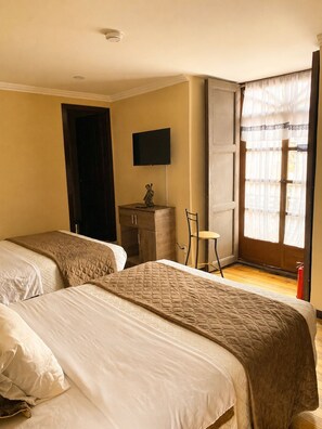 A hotel room with two beds, a television, a small table, and a window with curtains. - Melody Hotel (Cuenca)