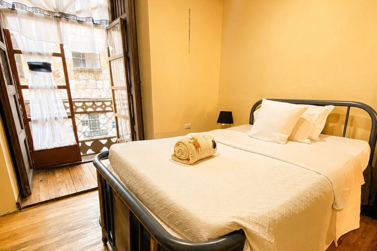 A bedroom with a bed, a nightstand, a lamp, and a window with curtains.