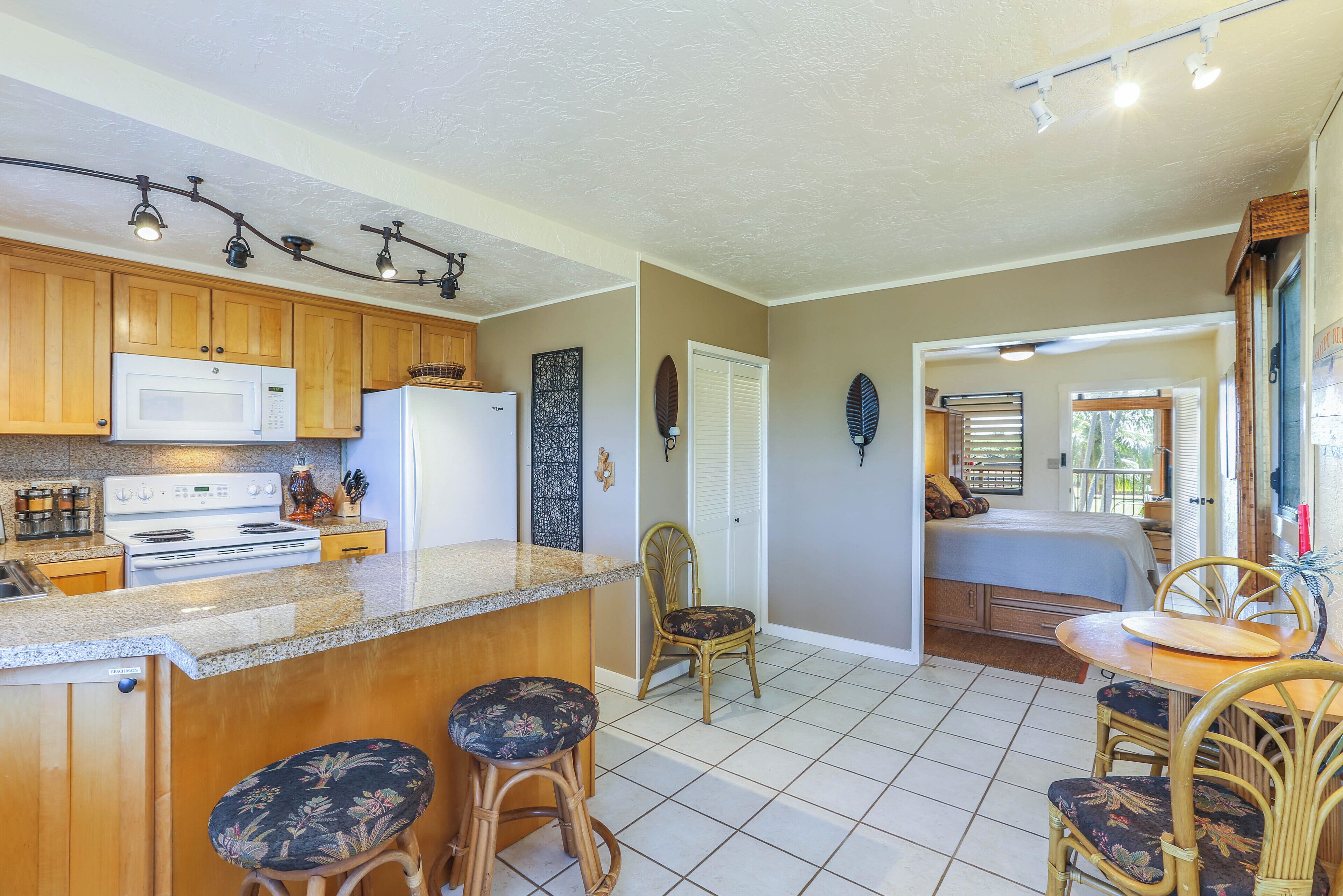 A kitchen with wooden cabinets, a microwave, and a refrigerator. There is a dining area with a table and chairs.