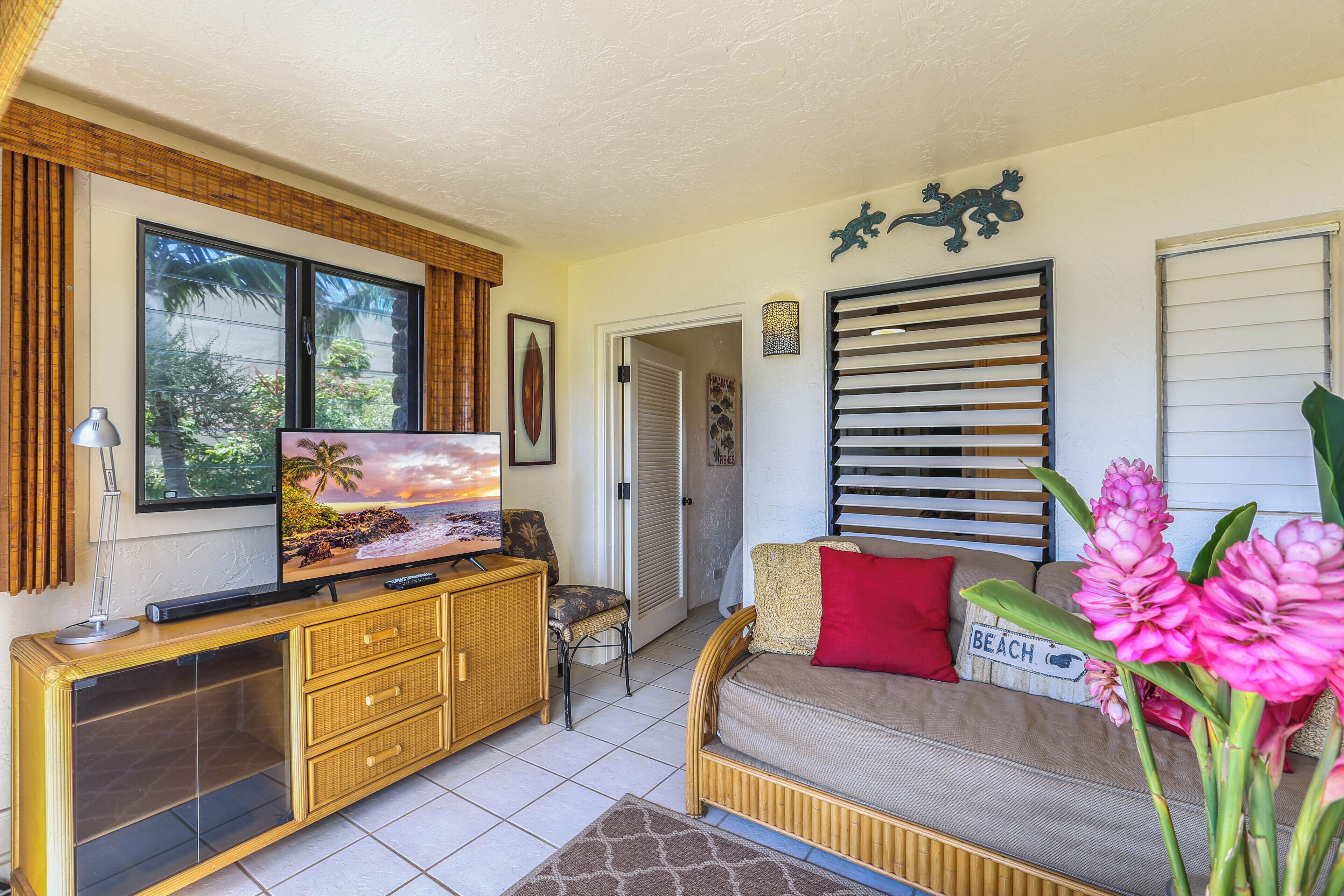 A living room with a television, a wicker console, a sofa with a beach-themed pillow, and a door leading to another room.