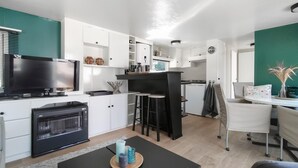 A modern kitchen with white cabinets, a black countertop, and a built-in oven. There is a dining area with a table and chairs, and a TV mounted on the wall. - Gorgeous home in Merksplas (Merksplas)