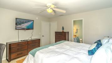 A bedroom with a bed, dresser, TV, and a ceiling fan.