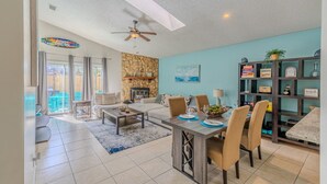 A spacious living room with a fireplace, a dining area with a table and chairs, and a bookshelf filled with books and decorative items. - Beach Retreat with Backyard Flair! w/Yard Games (Atlantic Beach)