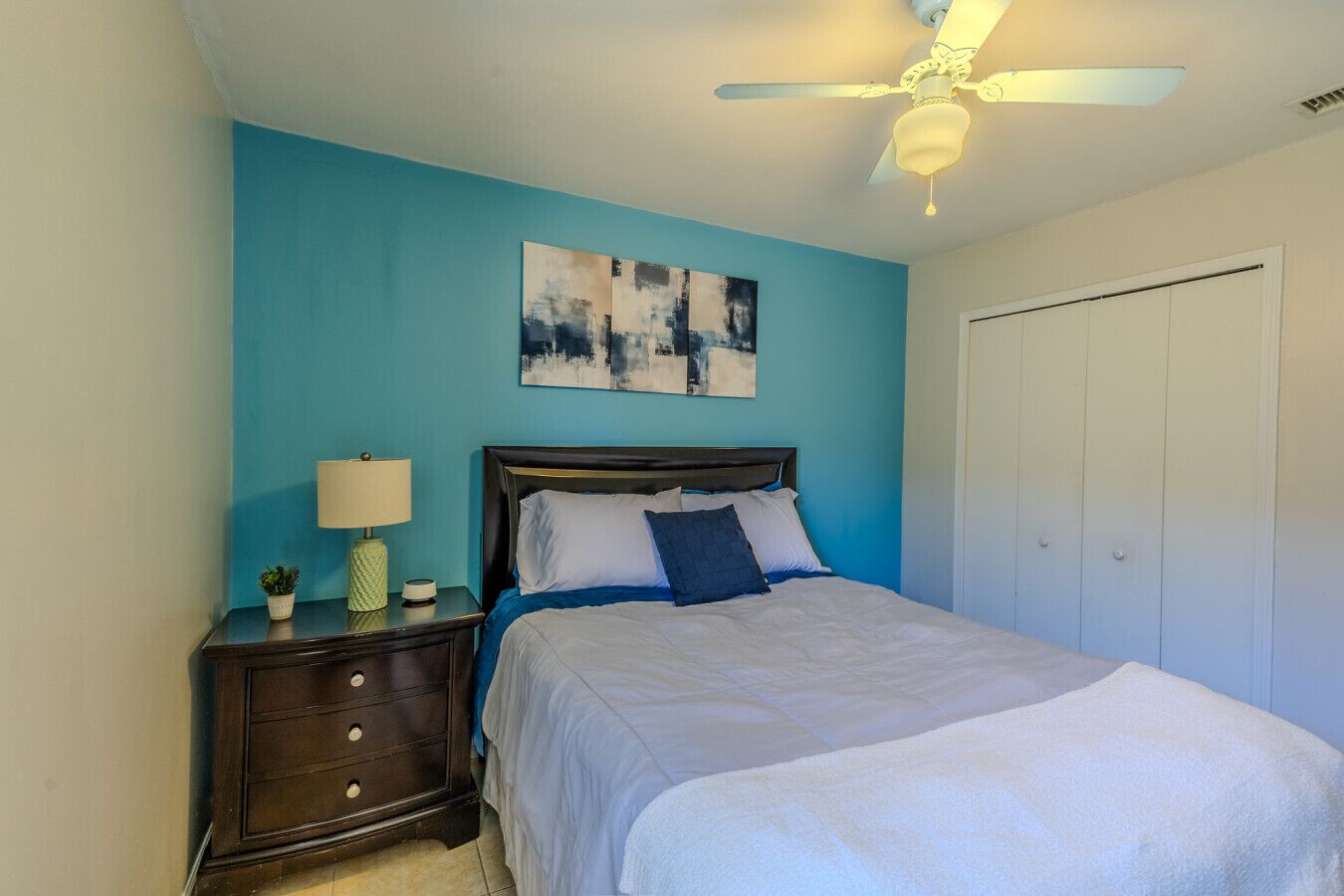 A bedroom with a bed, a nightstand, a lamp, a ceiling fan, and a door.