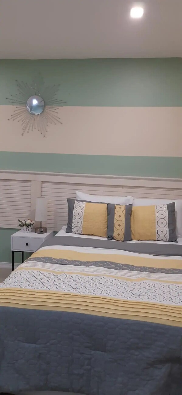 A neatly made bed with patterned bedding, a bedside table with a lamp, and a decorative wall piece.