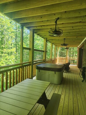 A wooden deck with a hot tub, ceiling fans, and a view of the forest.