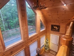 A cabin with large windows, a deer head chandelier, a Christmas tree, and a framed animal picture.