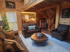 A log cabin interior with a living room, a dining area, and a staircase.
