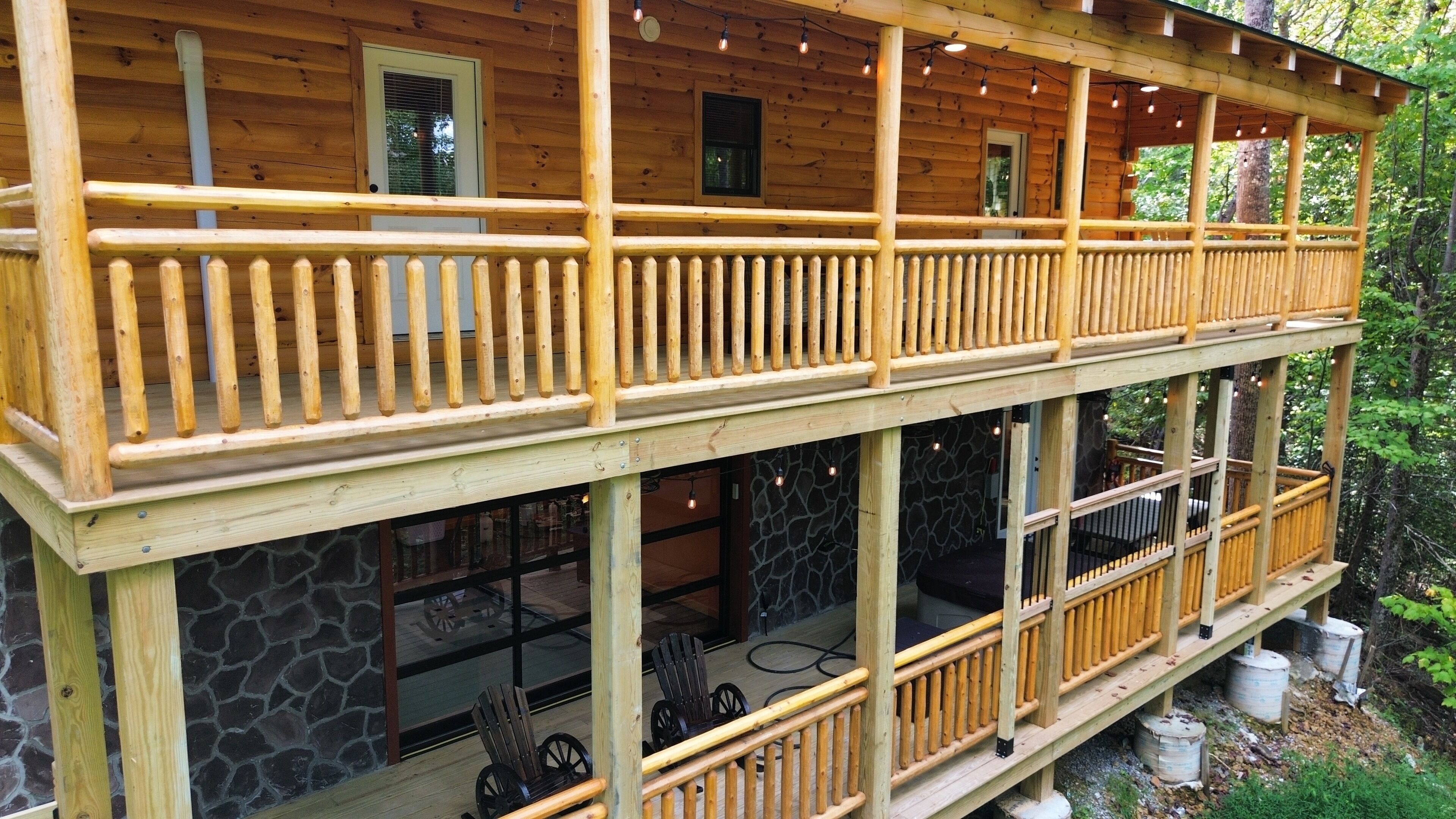 A two-story wooden cabin with a balcony, stone walls, and a stone fireplace.