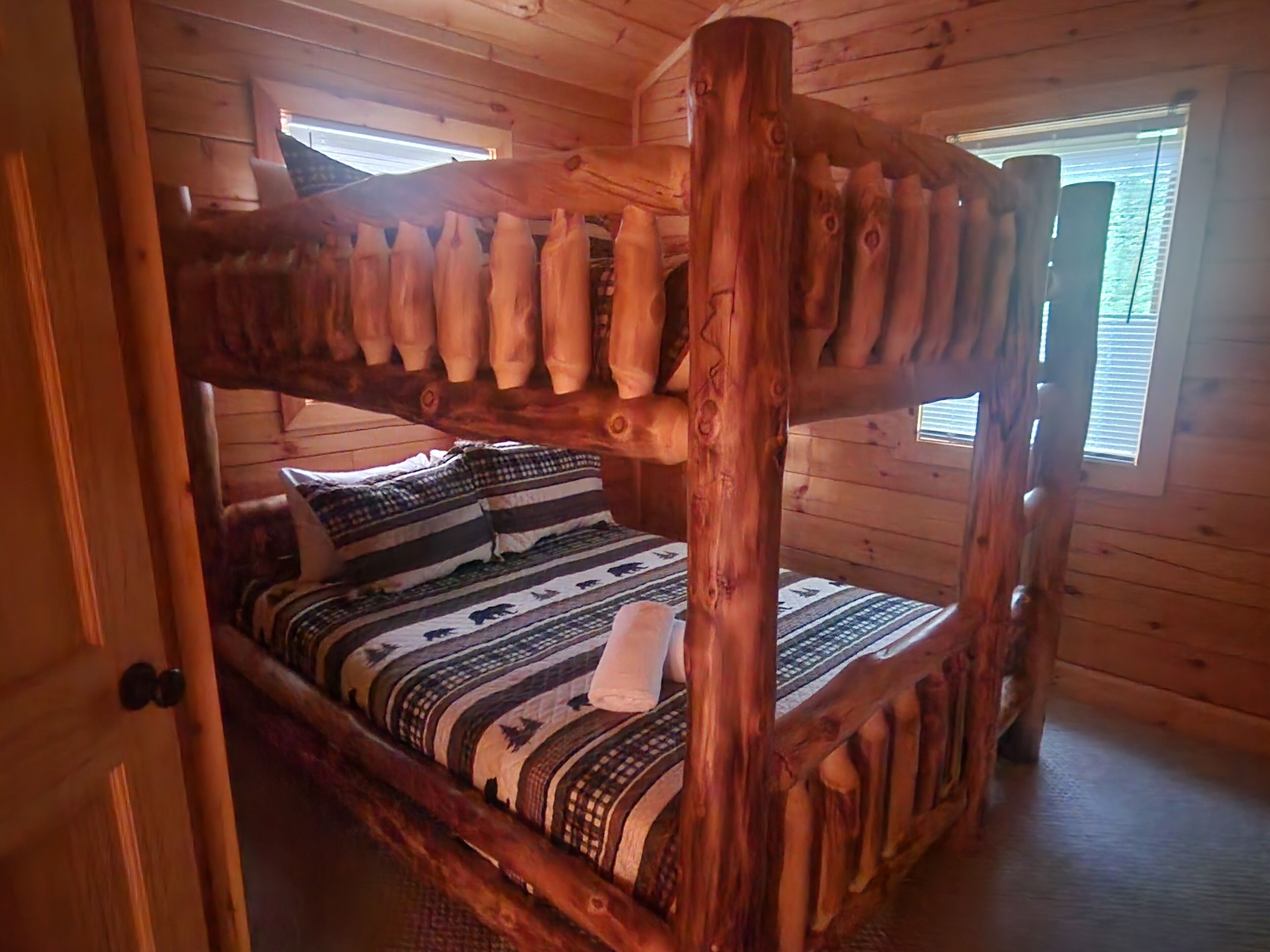 Uma cama beliche de madeira com escada, colcha estampada e travesseiros.