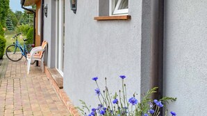 Une maison avec une allée pavée, un vélo, un banc et un parterre de fleurs bleues.