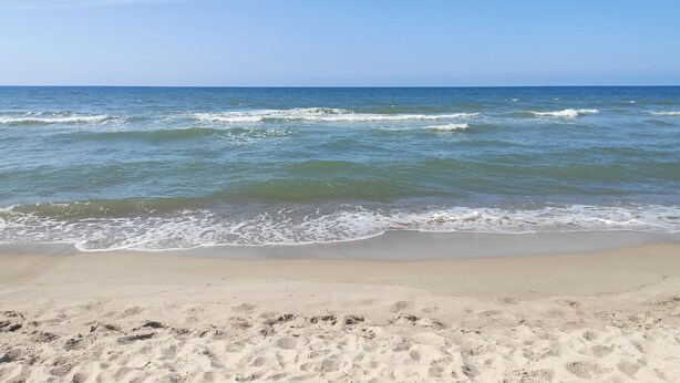 Une plage avec une eau d’un bleu limpide et un rivage sablonneux.