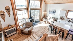 Amplia sala de estar con chimenea, ventanas grandes y cocina con taburetes de bar.