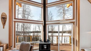 Interior acogedor de una cabaña con ventanas amplias, chimenea y vista a un paisaje nevado.