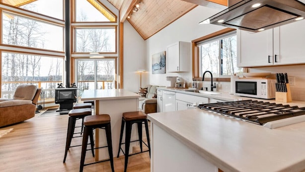 Una cocina moderna con una isla central, taburetes de bar, estufa y microondas.