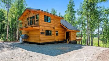 A two-story log cabin with a balcony, a covered porch, and a gravel driveway.