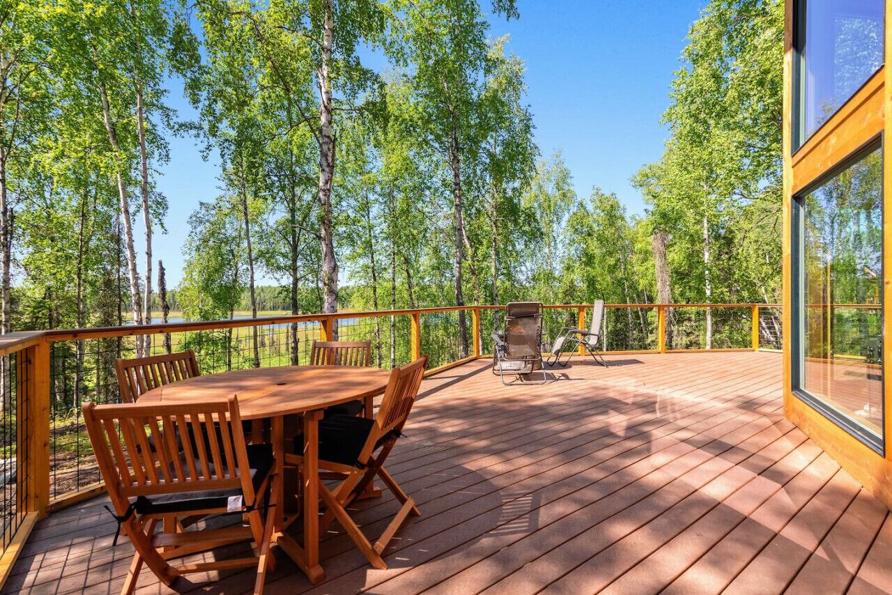 Een houten terras met een tafel en stoelen, met uitzicht op een bebost gebied.